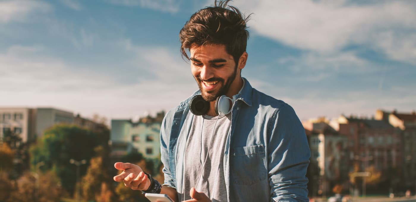 Man outdoors smiling while looking at his phone